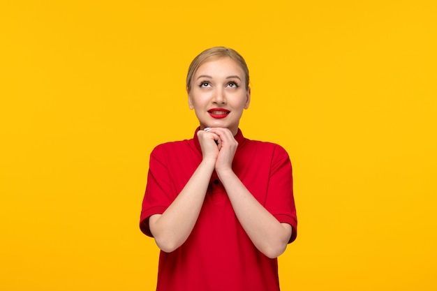 Ragazza carina giorno della camicia rossa che si tiene per mano mentre prega in una camicia rossa su sfondo giallo