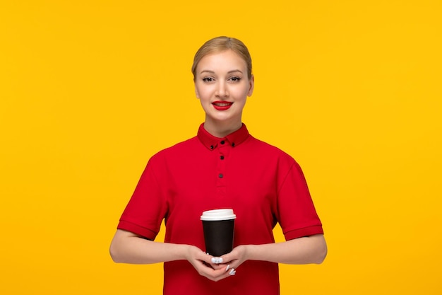 黄色の背景に赤いシャツでコーヒーカップを保持している赤いシャツの日のかわいい女の子