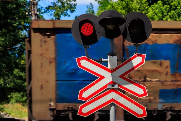 Красный сигнал семафора и знак остановки перед железнодорожным переездом с проезжающим поездом