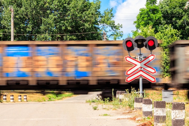 Red signal of semaphore and stop sign in front of railroad crossing with train passing