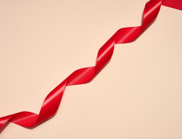 Red silk ribbon on a beige background top view