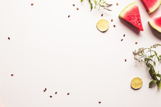 Red slices of ripe watermelon with mint leaves and lime slices on a white background. Top view, flat lay, copy space