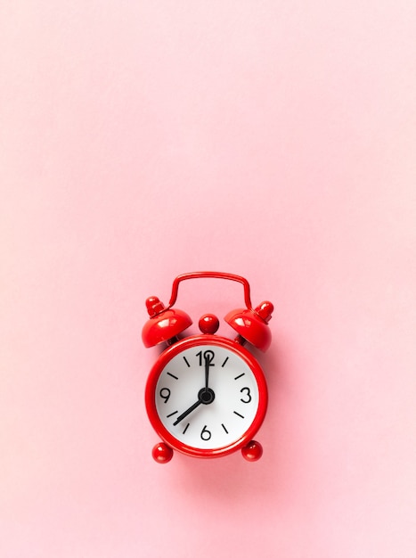 Red small alarm clock on pastel pink background