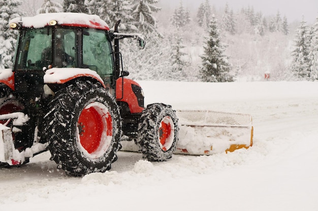 Red snowblower grader clears snow covered ski resort road in mountains or city street Winter snowflake snowfall weather Horizontal copy space