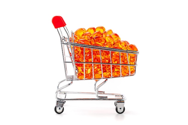 Red soft gel vitamin capsules in mini supermarket push cart isolated on white background, healthy and marketing concept