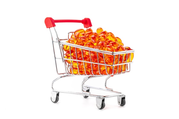 Red soft gel vitamin capsules in mini supermarket push cart isolated on white background, healthy and marketing concept