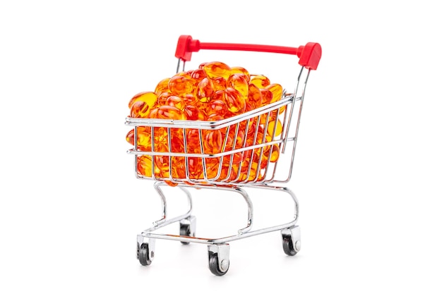 Red soft gel vitamin capsules in mini supermarket push cart isolated on white background, healthy and marketing concept