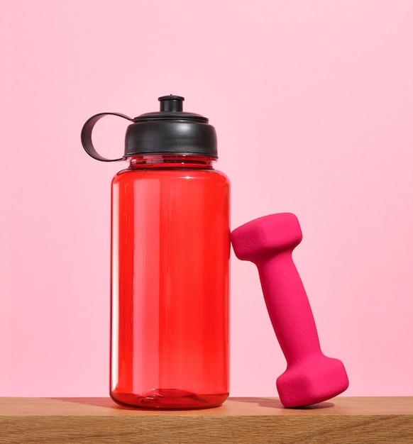 A red sports shaker for drinking clean water during workouts and a pink dumbbell Exercise workout