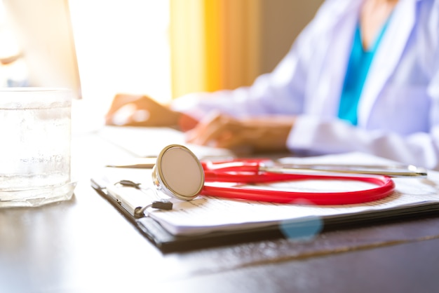 Red stethoscope on check list working table with female doctor hand working.