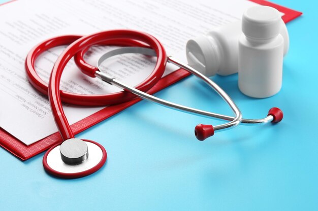 Red stethoscope and pills on blue background