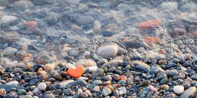 red stone in shape of heart on beach by sea