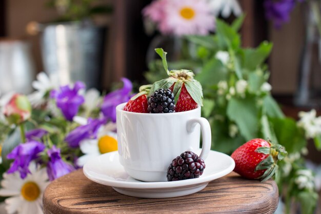 Red strawberries and blackberries in a cup on a wooden table against a background of bright colors Summer harvest in the village