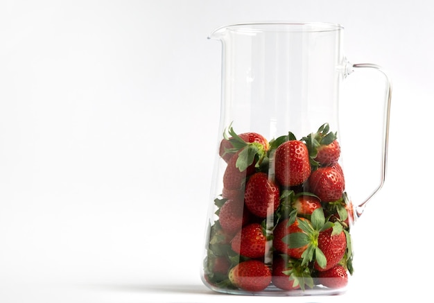 Red strawberriesin a glass jug on a white background with copy space for your text