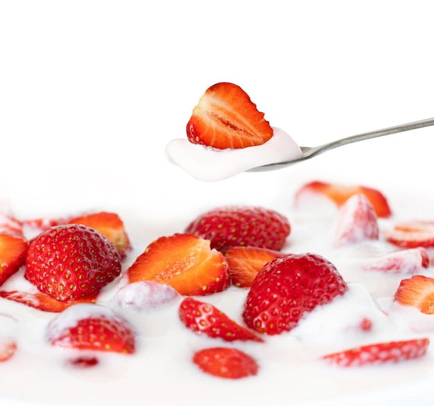 Red strawberry on a dessert spoon and yogurt with strawberries.