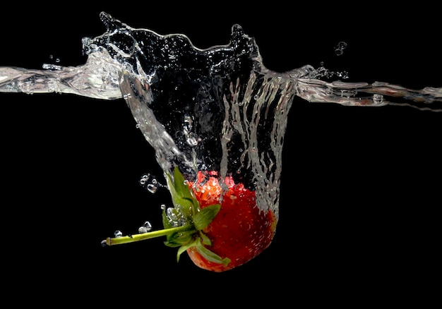 Foto fragola rossa in spruzzi d'acqua su sfondo nero