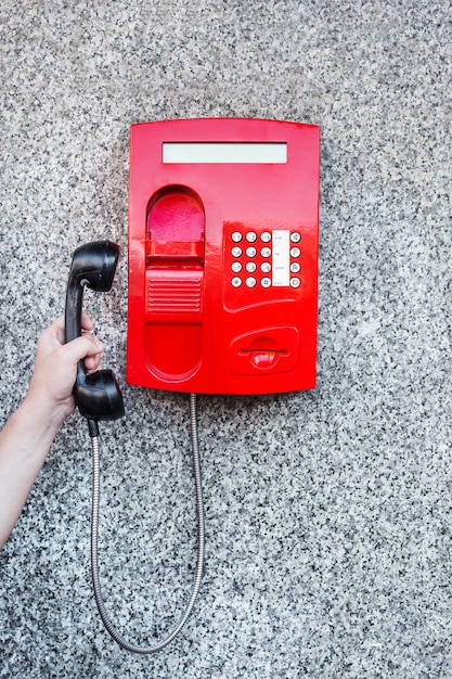 Red street pay phone on the wall and a man's hand picking up the phone