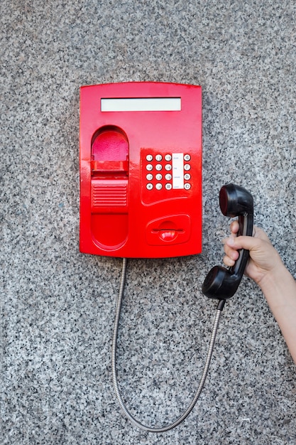 Photo red street pay phone on the wall and a man's hand picking up the phone