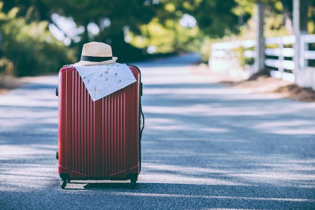 Red suitcase hat and map on the road in countryside Summer vacation and travel concept