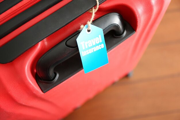 Red suitcase with label, closeup. travel insurance concept