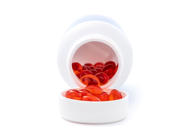 클리핑 패스가 있는 흰색 배경에 격리된 흰색 플라스틱 병에서 건강을 위한 빨간색 보충 캡슐이 쏟아져 나옵니다.