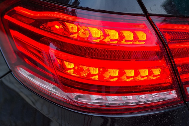 Red tail lights (rear lights, brake lights) of black car close\
up image.