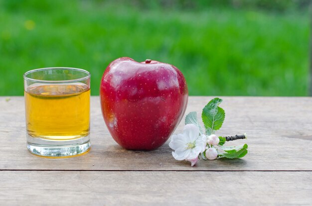 Red and tasty apples with a glass of cider (apple juice) on wooden table