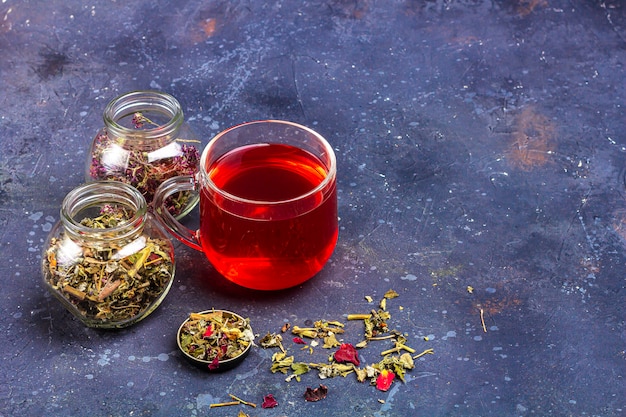 Red tea in glass cup and jars of dry tea leaf and petals