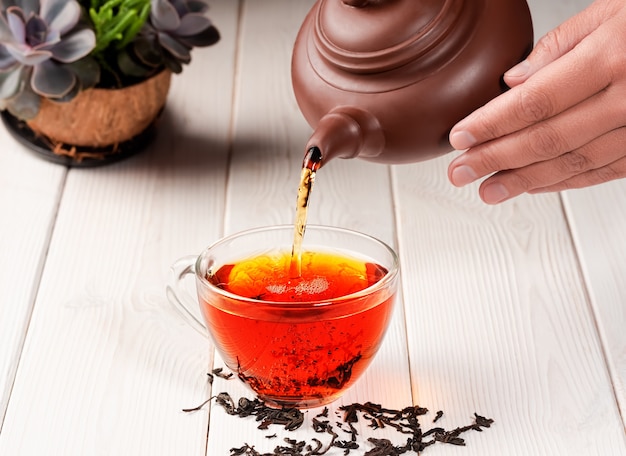 Photo red tea is poured into a glass cup from teapot