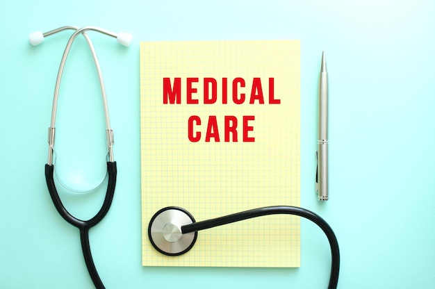 The red text MEDICAL CARE is written in a yellow pad that lies next to the stethoscope on a blue background