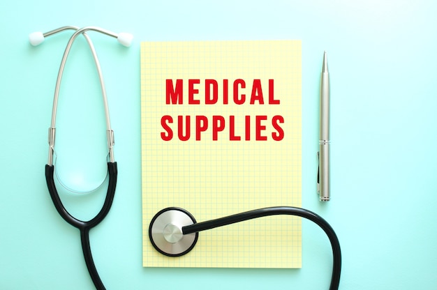 The red text MEDICAL SUPPLIES is written in a yellow pad that lies next to the stethoscope on a blue background.