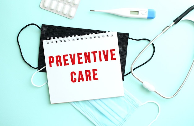 빨간색 텍스트 PREVENTIVE CARE는 의료 용품 옆 파란색 배경에 있는 메모장에 쓰여 있습니다.