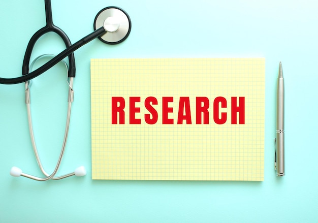 The red text RESEARCH is written in a yellow pad that lies next to the stethoscope on a blue background.