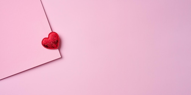 Red textile heart on a pink paper background top view