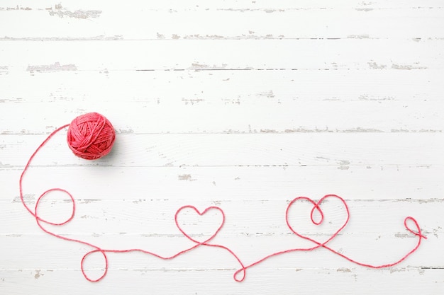 Red thread, two hearts and tangle on light wooden