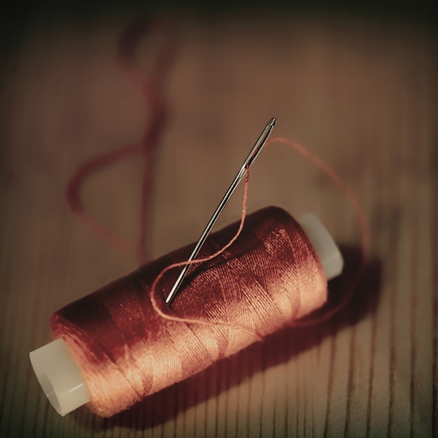 写真 木製の背景に対して針と赤い糸。トーンの写真
