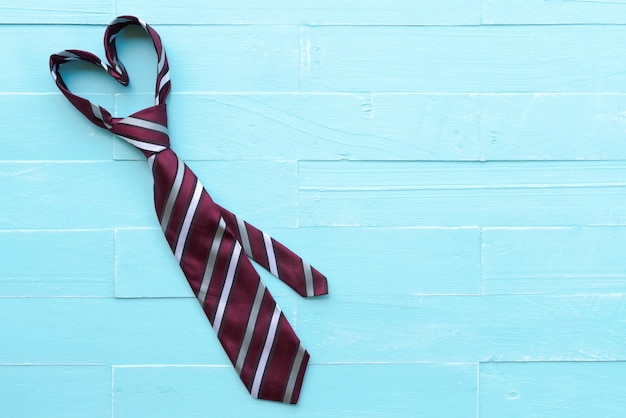 Photo red tie in heart shape on bright blue pastel wooden table background.