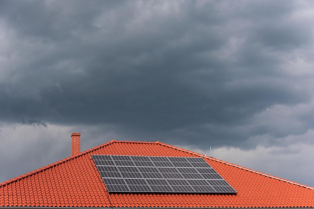 Foto tetto di piastrelle rosse con pannelli fotovoltaici durante il tempo tempestoso installazione fotovoltaica solare nuvole blu scuro