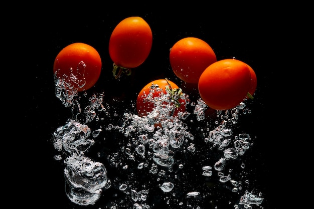 Red tomato on black background with water splash