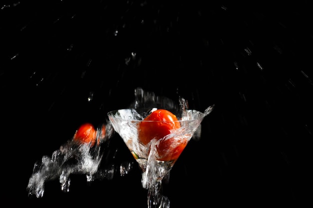 Red tomato falling down in glass with water