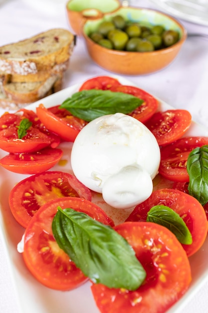 Red tomato salad with burrata cheese and fresh basil leaves Mediterranean style salad