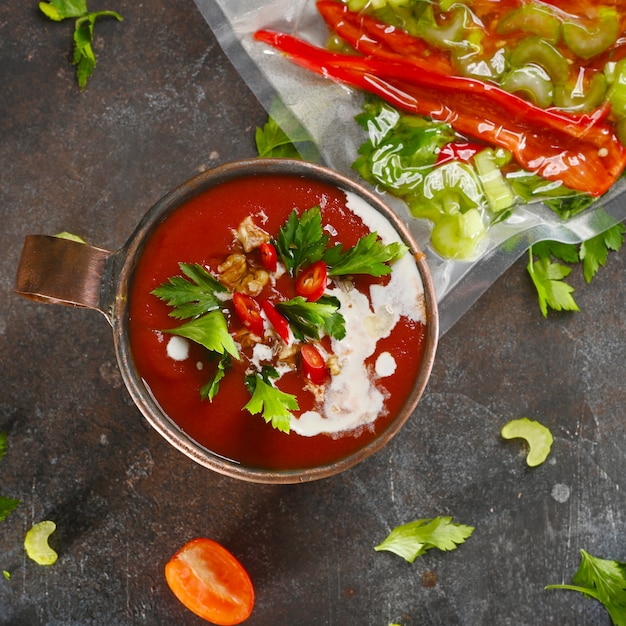 Minestra di pomodoro rossa in tazza di rame su oscurità.