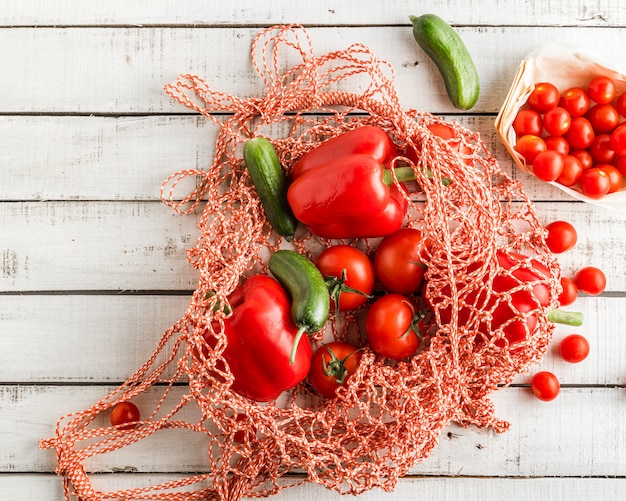 Pomodori e peperoni dolci rossi, cetrioli in una borsa di corda su fondo rustico bianco