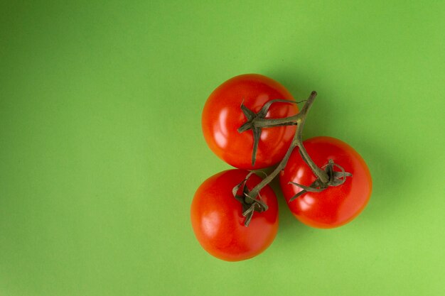 Red tomatoes on a branch on a green background view from above