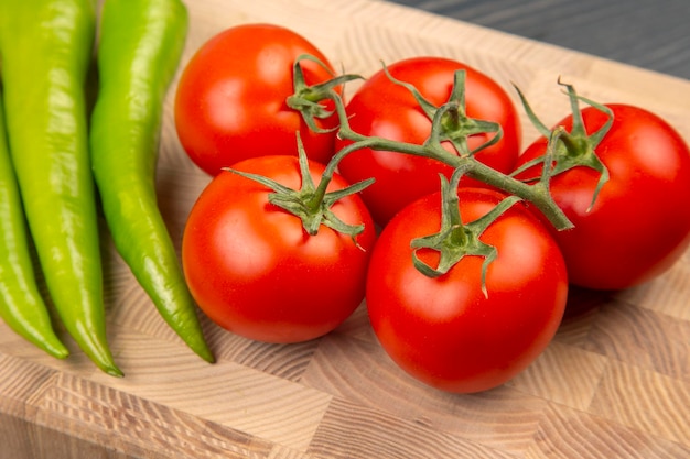 Red tomatoes and green hot peppers on a kitchen board