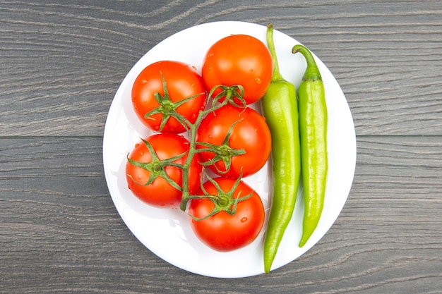 Red tomatoes and green hot peppers on a kitchen board