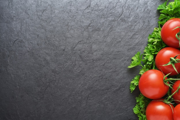 Red tomatoes and parsley on black slate with copy space