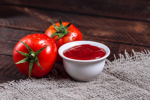 Red tomatoes and tomato sauce on a dark, wooden background.