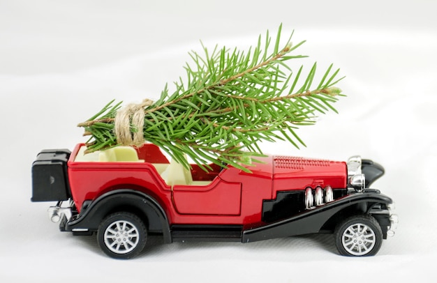 A red toy car carries spruce branches on a white blurry background Christmas Card background