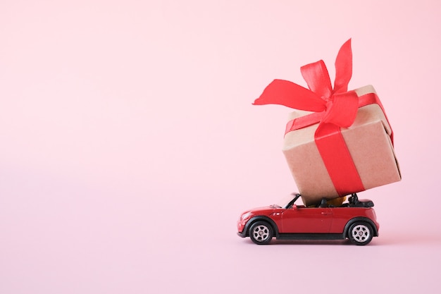 Automobile rossa del giocattolo che trasporta il contenitore di regalo con il nastro rosso