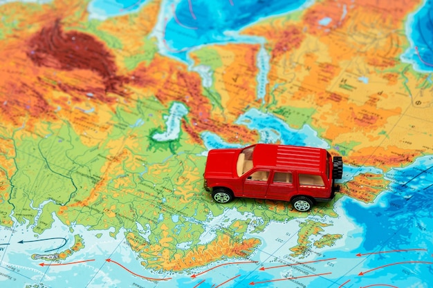 Red toy car on the physical map of the world in Europe towards the east